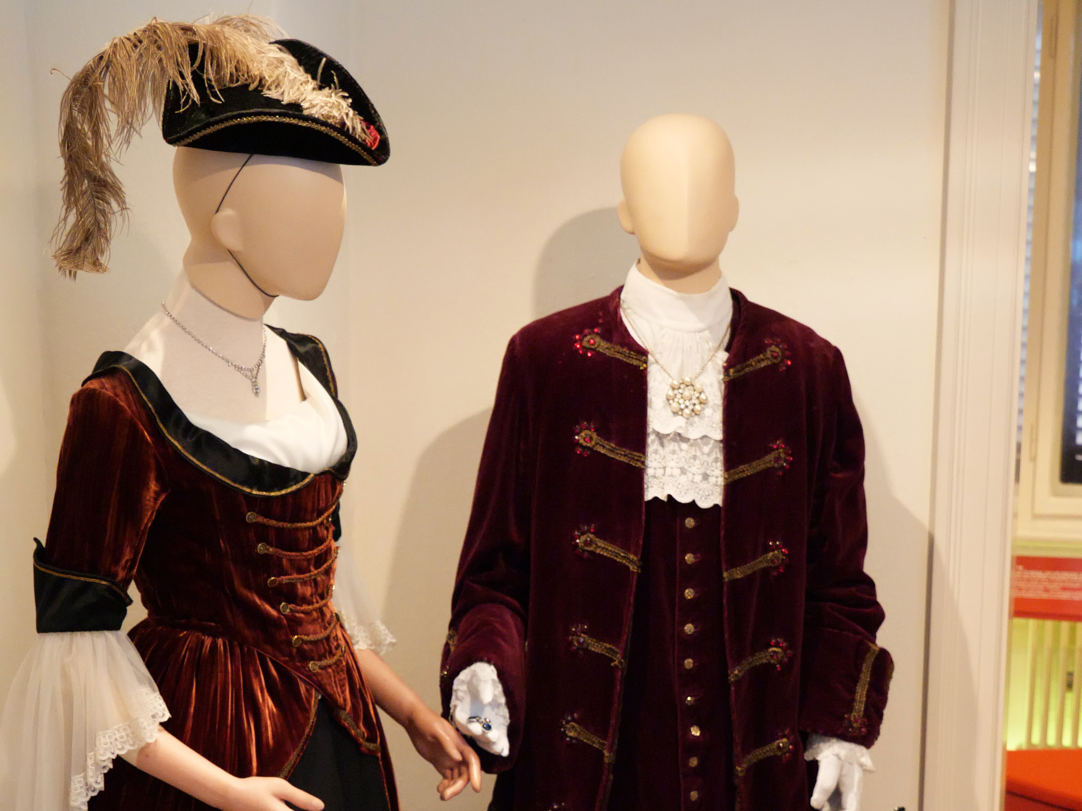 AI generated: The image shows two mannequins dressed in historical costumes, including a dress and a suit made of a red, velvet-like fabric. The clothes appear to be from an earlier era and are on display in an exhibition.