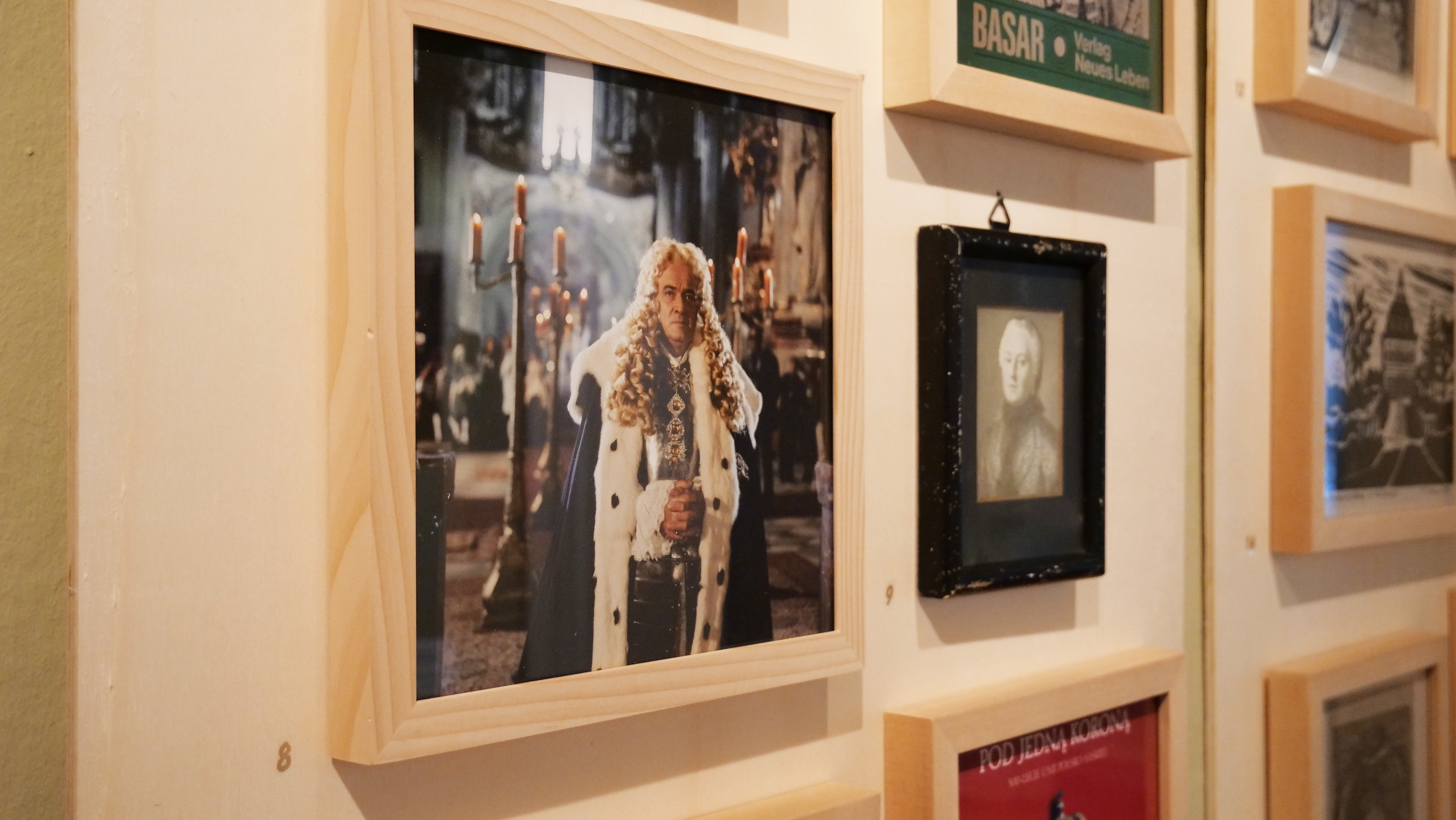 KI generiert: Das Bild zeigt eine Fotogalerie an einer Wand, wobei das zentrale Bild eine mit Kerzen beleuchtete Person in einem prächtigen, königlichen Gewand darstellt. Der Fokus liegt auf diesem Foto, das von mehreren anderen Bildern umgeben ist.