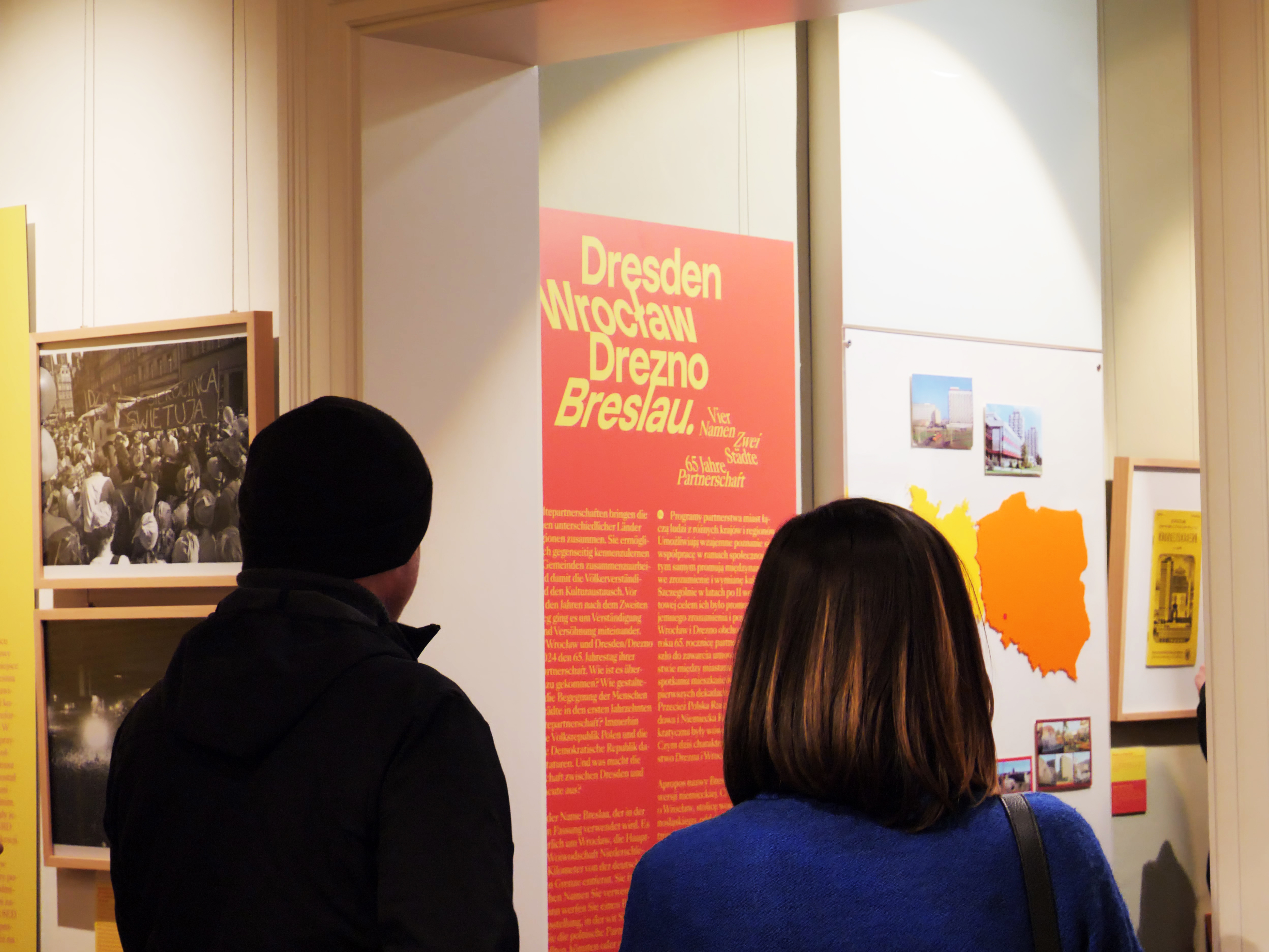 KI generiert: Das Bild zeigt zwei Personen, die sich eine Ausstellung über die Städtepartnerschaft zwischen Dresden und Breslau ansehen. Auf einer Tafel sind die Namen der Städte gut sichtbar hervorgehoben.