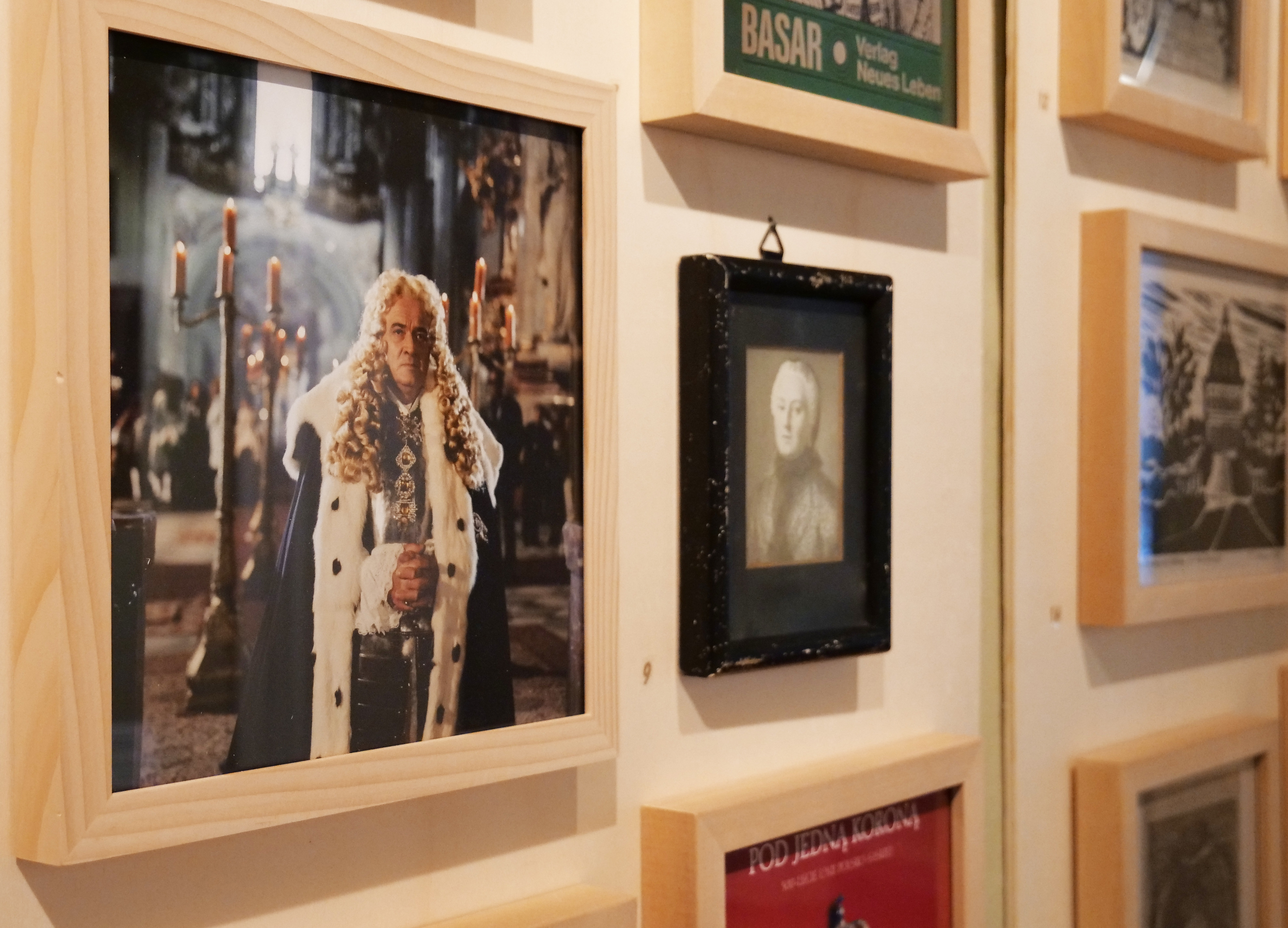 KI generiert: Das Bild zeigt eine Fotogalerie an einer Wand, wobei das zentrale Bild eine mit Kerzen beleuchtete Person in einem prächtigen, königlichen Gewand darstellt. Der Fokus liegt auf diesem Foto, das von mehreren anderen Bildern umgeben ist.